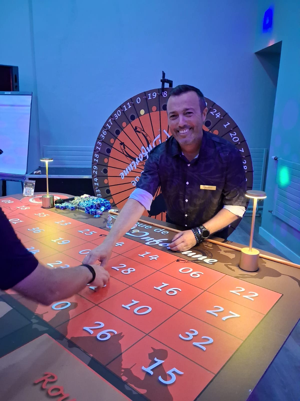 Croupier souriant présentant la Roue de l'Infortune lors d'un événement d'entreprise à La Pommeraye.