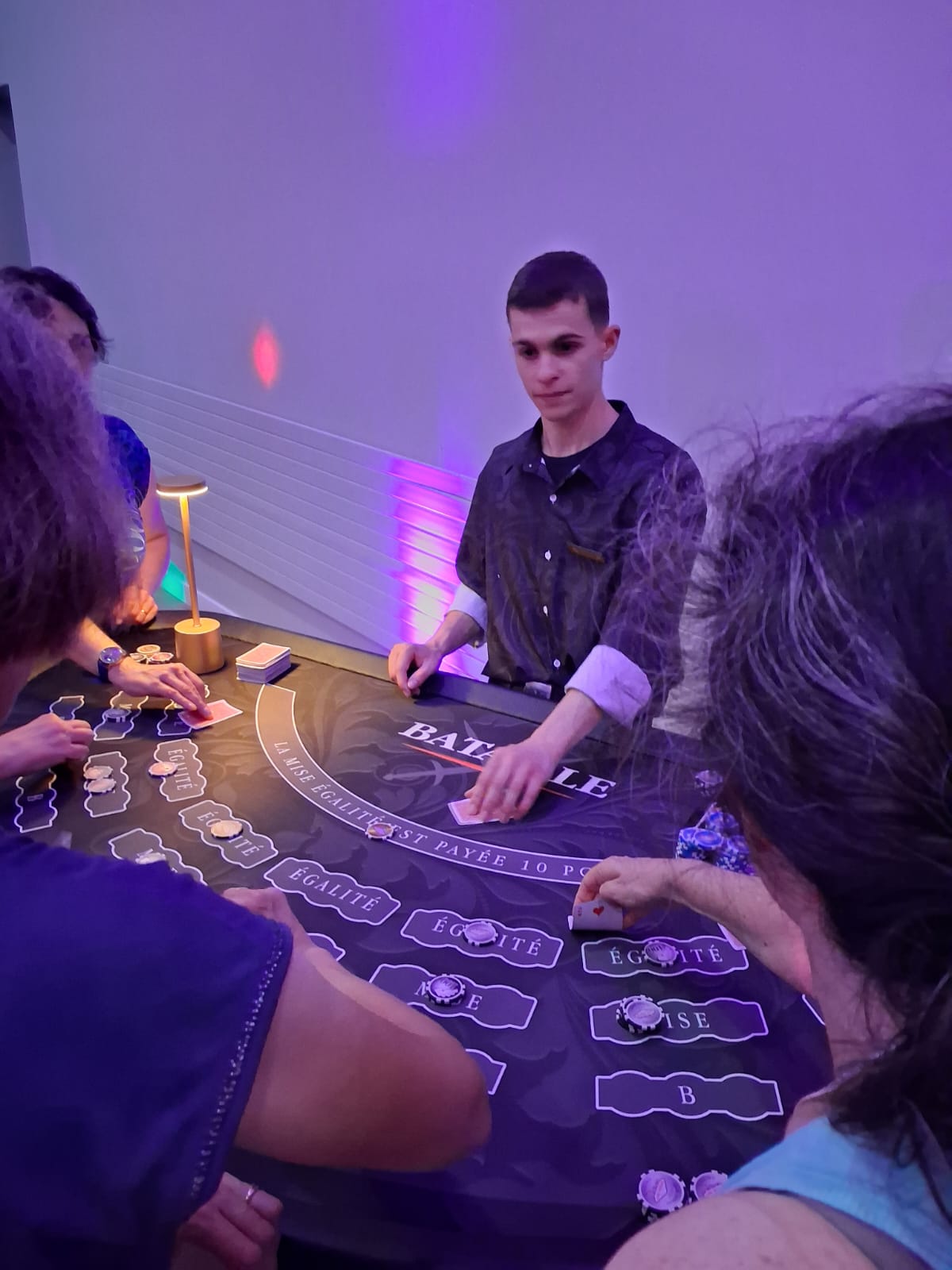 Jeune animateur distribuant les cartes à la table de Bataille sous des jeux de lumières violets en soirée corporate.